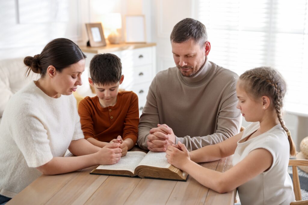 Family,With,Bible,Praying,At,Table,Indoors